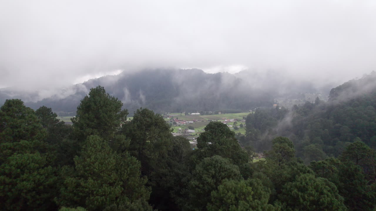 vuelo aéreo a través de nubes y árboles revelando una pequeña ciudad rodeada de montañas en el valle de bravo, méxico