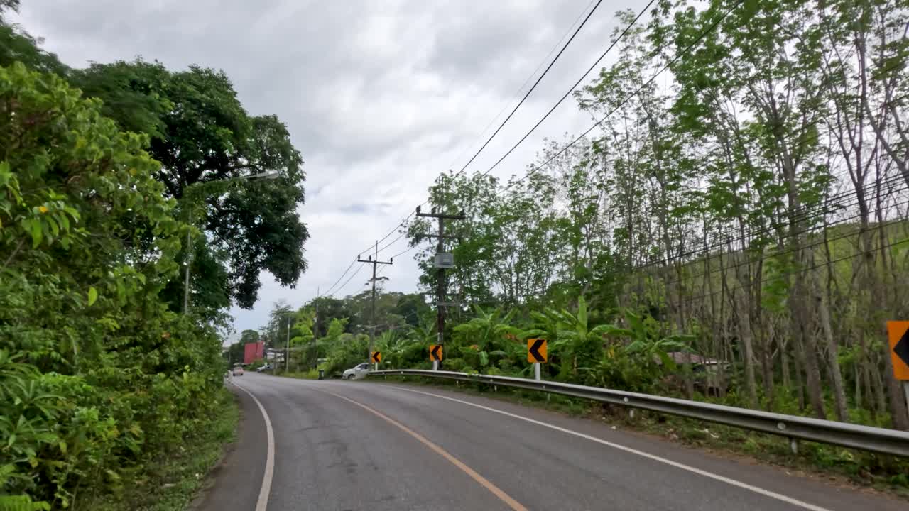Vehicle travels winding asphalt road through lush tropical landscape under overcast sky, steady forward motion