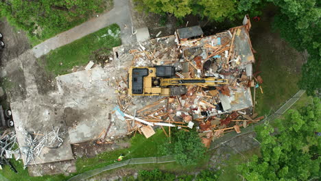 northampton, massachusetts, united states - an excavator demolishes an old house while a man sprinkles water to control dust - aerial topdown shot