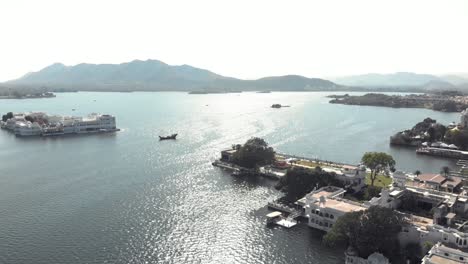 Vista-Panorámica-Desde-Ambrai-Ghat-Sobre-El-Lago-Pichola-Y-El-Palacio-Del-Lago-Taj-En-Udaipur,-Rajasthan,-India---Toma-Panorámica-Aérea