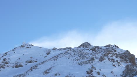 Snow-blowing-over-rocky-mountains-sunny-day-high-in-the-alps---pan-view