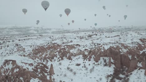 Areal-video-shoot-of-winter-landscape-filled-with-hot-air-balloons,-flight-over-hills-covered-with-snow