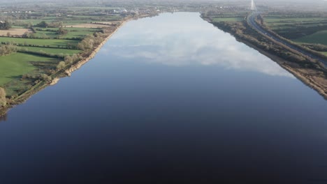 Bucolic-rural-scene:-Green-pastures-by-river-reflecting-sky-and-cloud