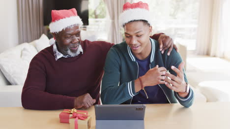 Happy-african-american-father-and-adult-son-in-christmas-hats-having-tablet-video-call,-slow-motion