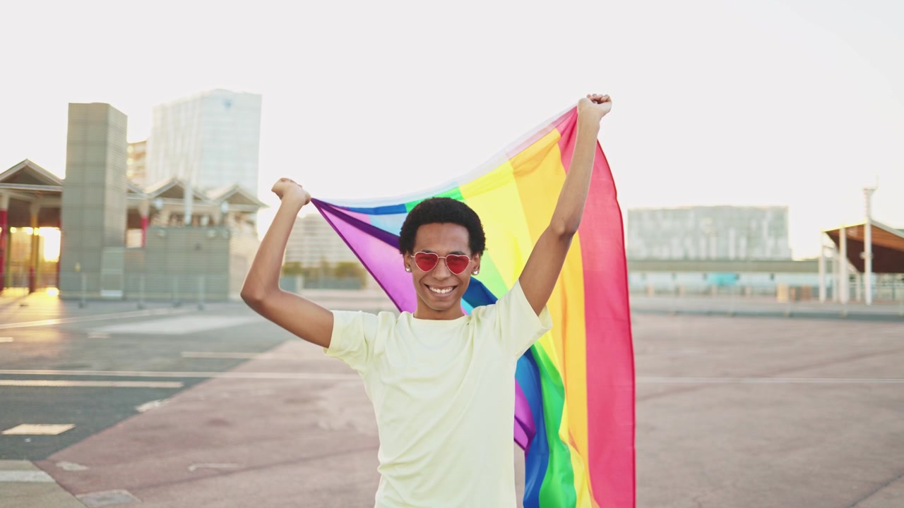 Proud Young Man Smiling and Waving Rainbow Pride Flag