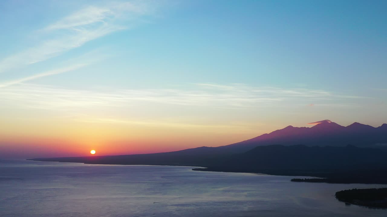 Pink yellow and blue sky at beautiful romantic sunset reflecting on sea surface with sun hiding behind mountains of tropical islands in Bali