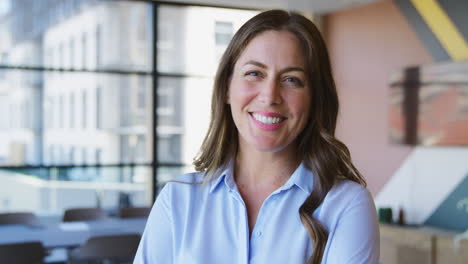 Portrait-Of-Smiling-Mature-Businesswoman-Standing-In-Empty-Office