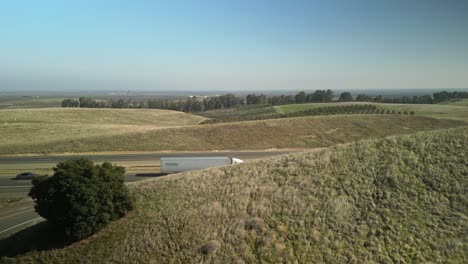 a drone view above highway 5 near newman, showcasing the highway cutting through endless fields, scattered farmsteads, and golden california landscapes.