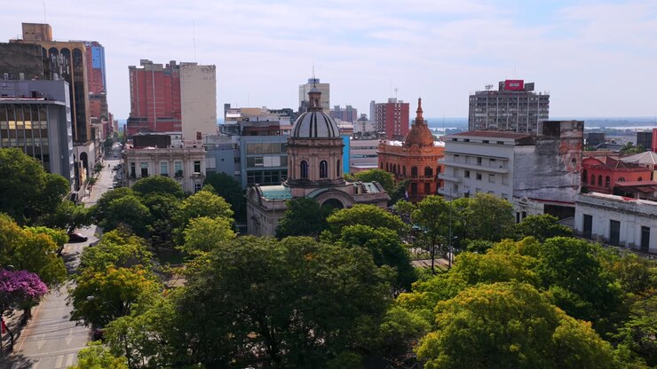 Drone video capturing sweeping views of Asuncion's Pantheon of Heroes. The lush greenery contrasts with historic and modern architecture under bright daylight.