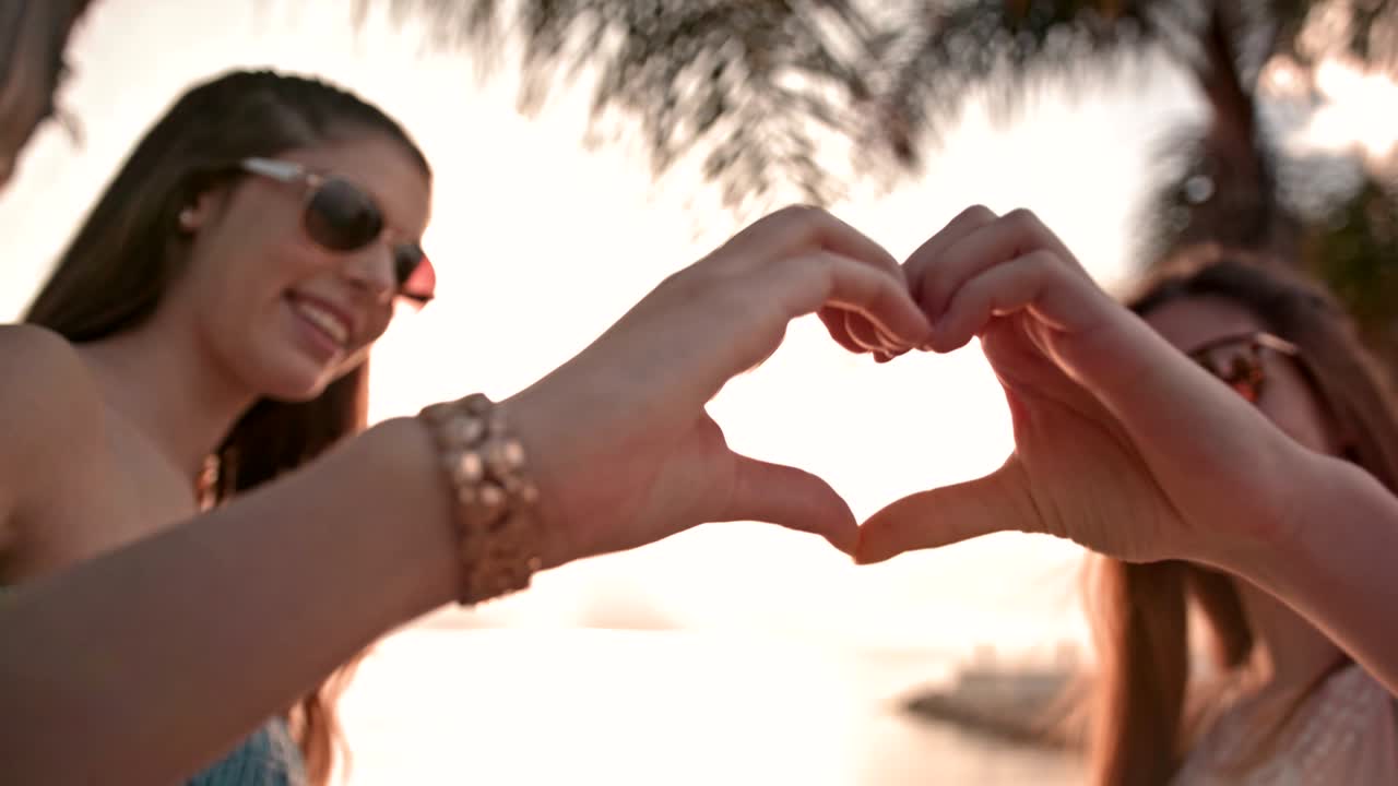 십대 소녀 들 이  나무 해변 에서 심장 모양 의 표지판 을 만들고 있다