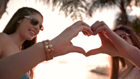 niñas adolescentes haciendo un letrero en forma de corazón en la playa de las palmeras