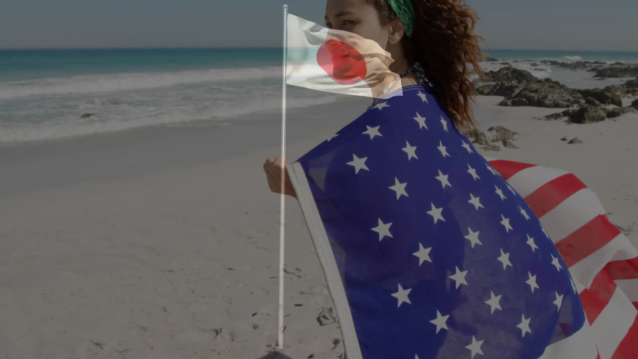 Standing on beach, woman wrapped in star-patterned flag with Japanese flag waving