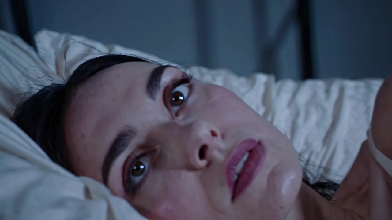 Close-up video shot of a woman's face lying on a pillow, capturing her wide-eyed expression