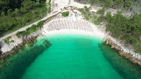 aerial view slowly tilting down to reveal the beautiful marble beach, with crystal clear water, white pebbles and lush green vegetation, umbrellas, thassos island, greece, mediterranean sea, europe