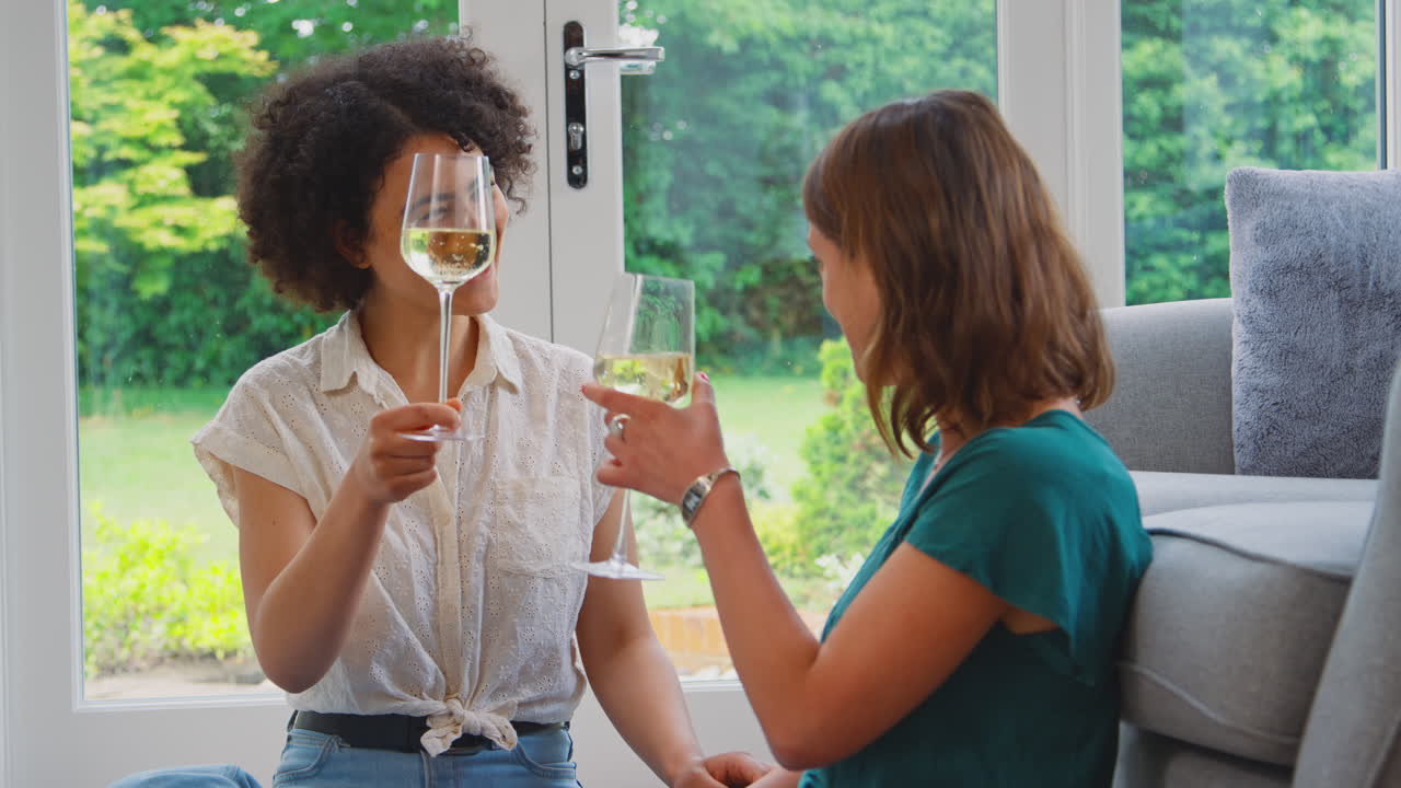 Same Sex Female Couple Or Friends At Home Relaxing In Lounge Drinking Wine Together