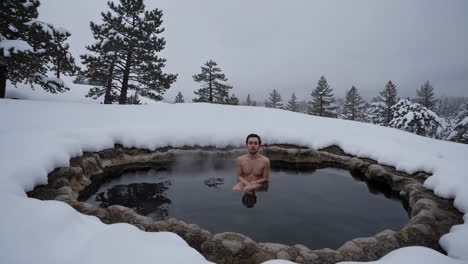 man relaxing in a steaming hot spring surrounded by snow in winter