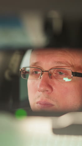 a close-up shot captures a man s face reflected in a car s rearview mirror, showing a focused and serious expression. the man is wearing glasses