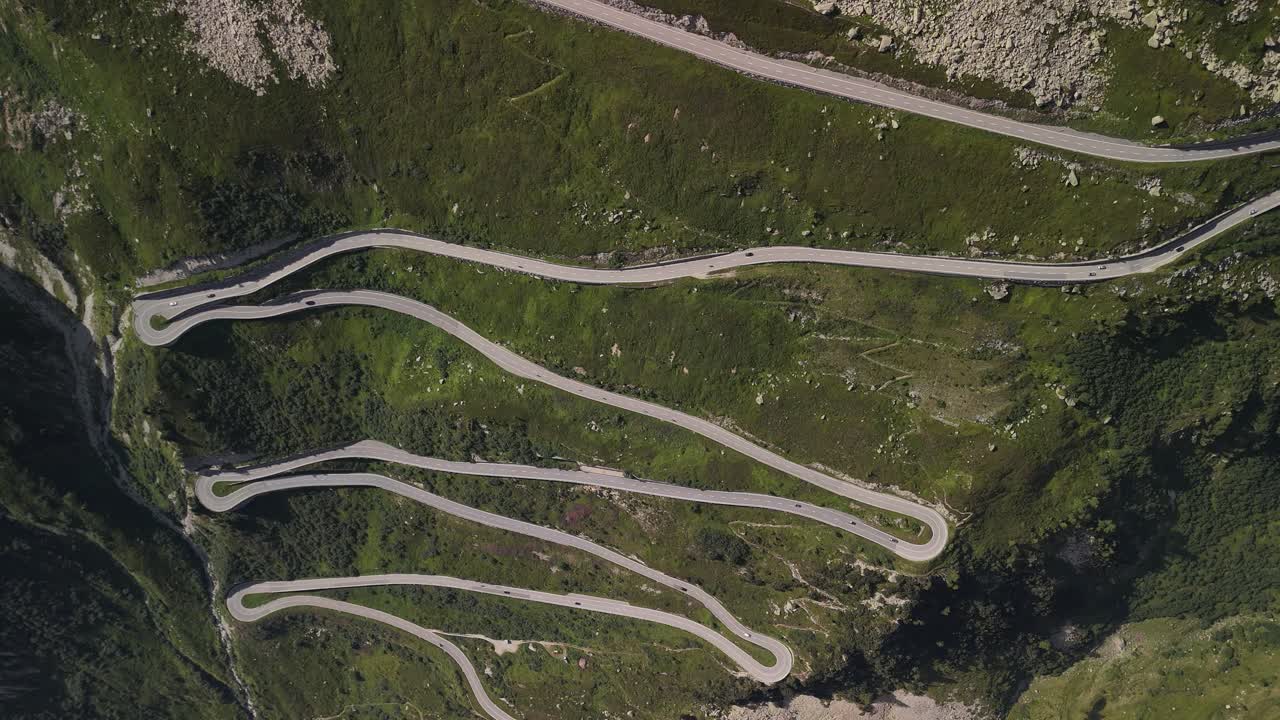 Top-down aerial view of serpentine roads winding through the mountainous region near Lake Totensee in Obergoms, Switzerland, illustrating the intricate path through the rugged alpine terrain.