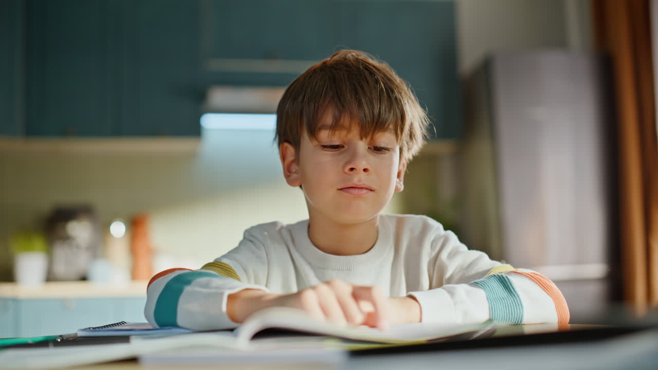 Scolaro risolve compito scolastico, pensa all'argomento, seduto alla scrivania della cucina di casa, primo piano