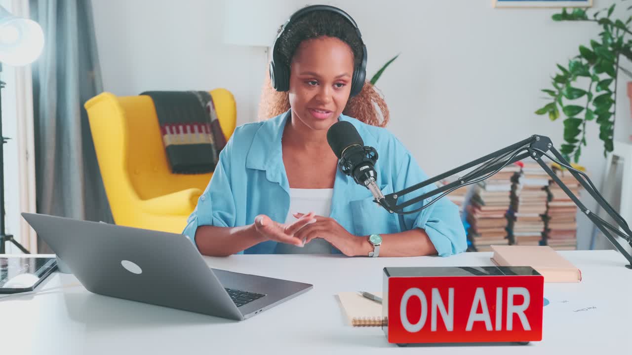 una joven bloguera afroamericana sociable se sienta en la mesa con un micrófono