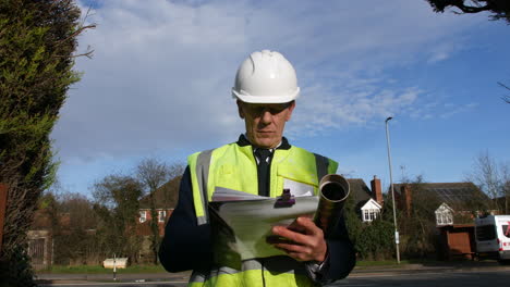 low angle portrait of an architect senior building construction manager on a residential street with traffic and houses looking at paperwork inspecting the building