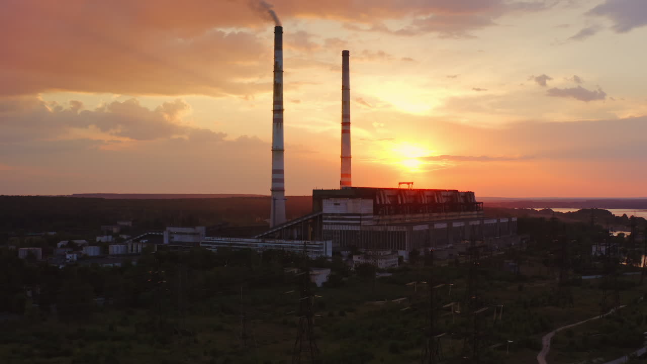 Factory in the evening. Dirty emissions from industrial pipes filling the air at sunset. Ecological problems. Aerial view. Camera rising up.