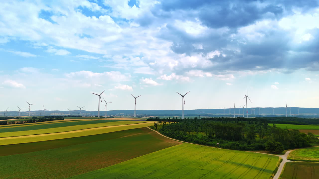 Lots of wind turbines rotate in the vast field in summer. Drone footage approaching wind mills at the backdrop of cloudy sky