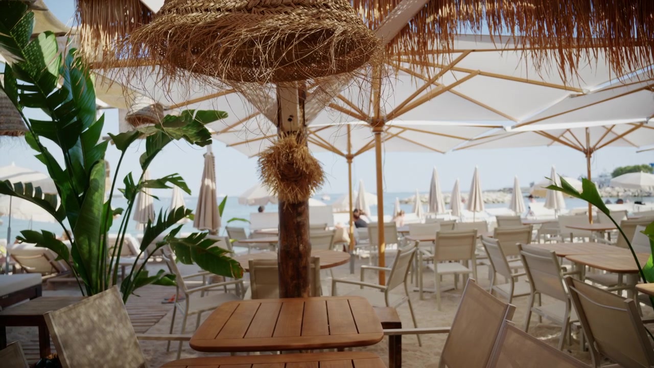 Ampia inquadratura di una terrazza elegante di un beach club con decorazioni in paglia, ombrelloni bianchi, piante tropicali e vista sull'oceano