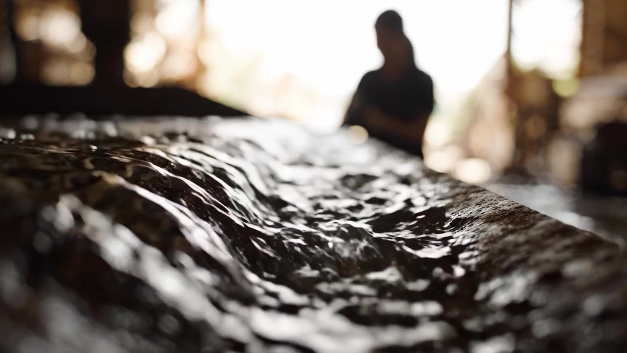 Silhouette di un operaio sullo sfondo con acqua che scorre in primo piano, catturando il contrasto tra movimento e immobilità in un ambiente industriale