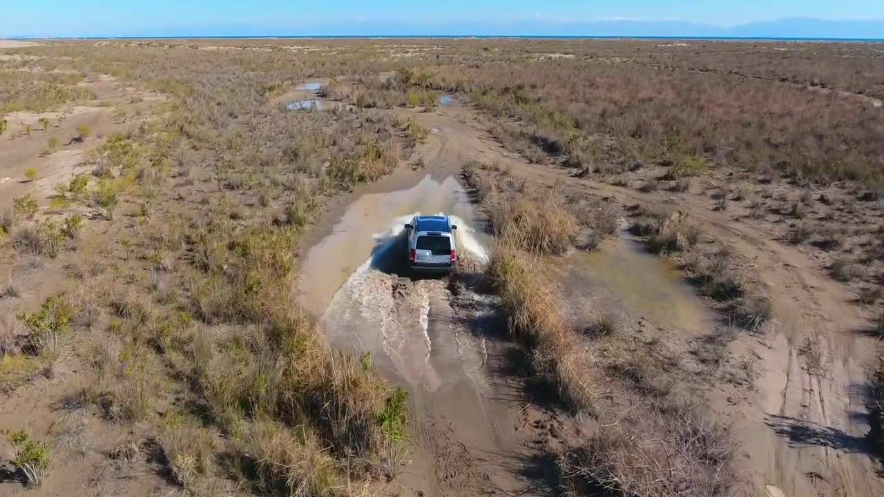 Silver SUV Driving Through Muddy Puddles in Desert Landscape