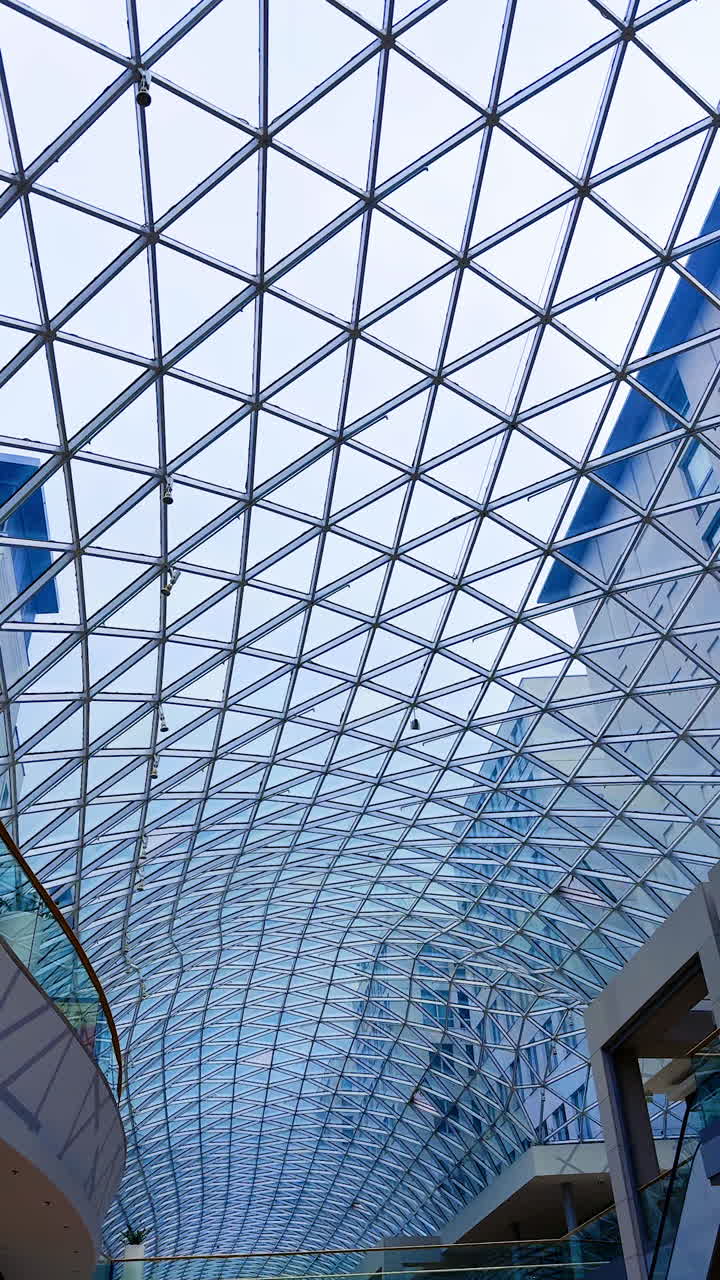 Modern architectural glass roof design. A striking glass ceiling structure showcases intricate geometric patterns above a shopping area in an urban setting