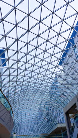 modern architectural glass roof design. a striking glass ceiling structure showcases intricate geometric patterns above a shopping area in an urban setting