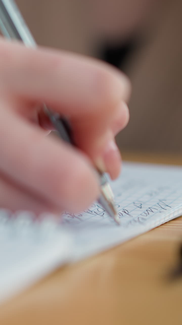 primer plano de la mano de la dama escribiendo con una pluma, mostrando el enfoque en el cuaderno, la cubierta de la pluma se encuentra en la mesa al lado, capturando una escena de estudio tranquila