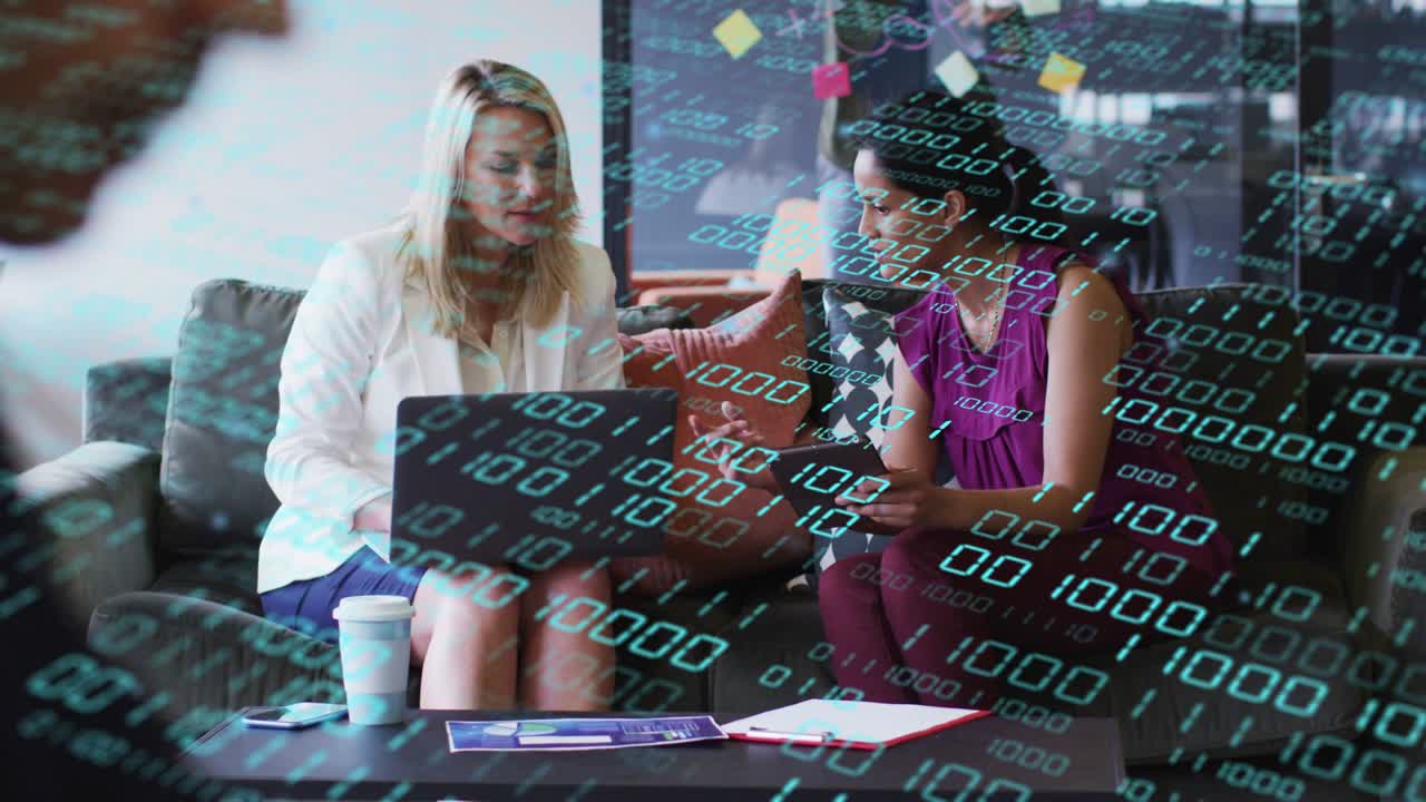 Two women working in lounge right woman pointing at laptop, reviewing business data with teal code