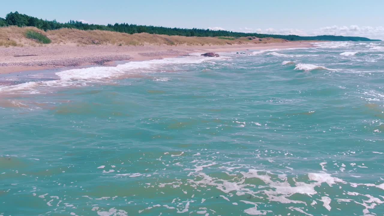 vista aérea baja volando por encima de las olas de agua turquesa chocando contra la orilla
