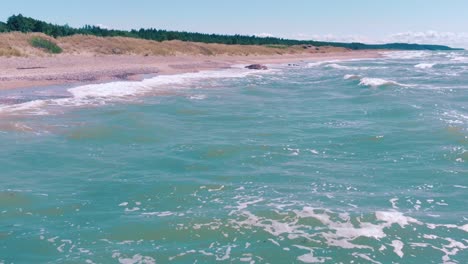 Low-aerial-view-flying-above-turquoise-water-waves-crashing-against-shore