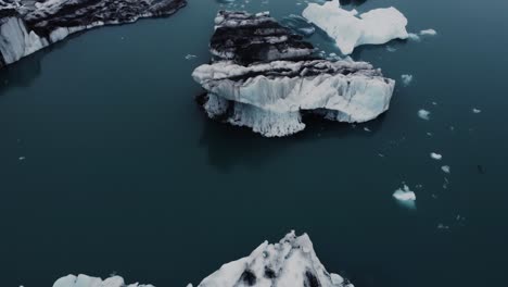 receding drone shot of beatiful black and white icebergs floating in a lagoon in iceland and birds flying by