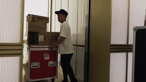 young asian man loading cases into a lift and the doors closing behind him