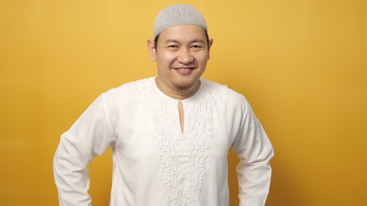 행복한 아시아 무슬림 젊은이가 노란색 배경에 미소 짓고 카메라에 포즈를 취하고 있습니다.