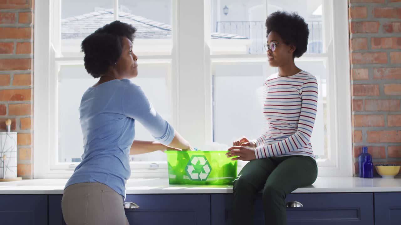 Happy african american mother and daughter recycling together in kitchen