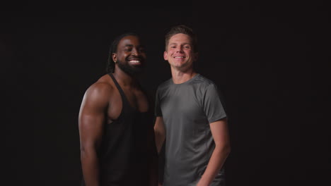 retrato de estudio de amigos masculinos atléticos sonrientes en ropa de fitness entrenando puño golpeando disparo contra fondo negro