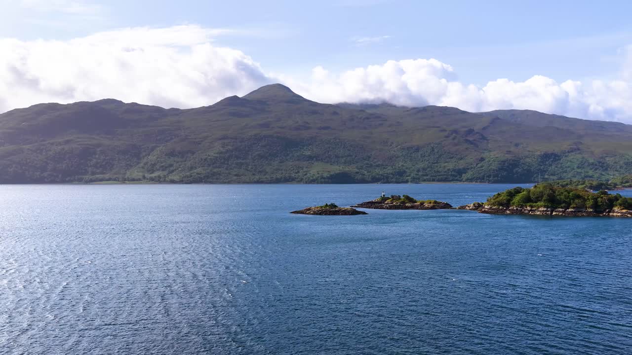 Camera slowly pans across tranquil lake, forested islands, and distant mountains under bright daylight