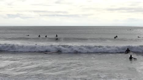 los surfistas remar y empujar a través de las olas entrantes - scarborough bay, christchurch, nueva zelanda