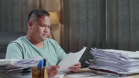 close up of fat asian man thinking then taking note while working with documents at the office