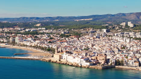 Un-Dron-Captura-Una-Antigua-Ciudad-Costera-En-Un-Clima-Soleado-Y-Con-Un-Telón-De-Fondo-Montañoso