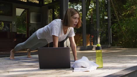 mujer asiática practicando yoga al aire libre en el jardín con computadora portátil