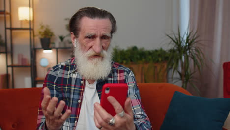 Senior-grandfather-man-making-phone-conversation-call-with-family-sitting-on-couch-at-home-in-room