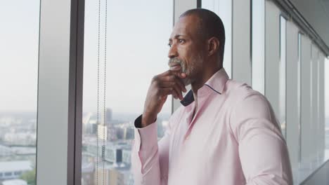 thoughtful professional businessman looking out of a window while his hand on his chin in slow motio