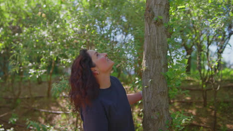 woman enjoying the outdoors, touching a tree trunk.