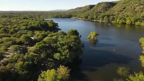 People-paddling-on-yellow-kayak-towards-verdant-lake-shores-of-Cordoba-in-Argentina